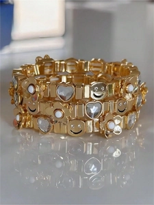 Detail of three stacked gold bracelets with diamond smiles, hearts and pearl flowers
