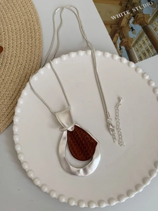 Silver long snake chain necklace with brown wood inlay teardrop pendant on white plate