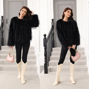 Veste courte en fausse fourrure noire portée avec des bottes dans un décor extérieur chic