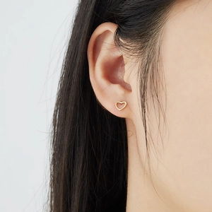 Close-up of minimalist golden hollow heart stud earring worn on model's ear