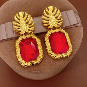 Gros plan de boucles d'oreilles feuille dorée avec cristal rouge rectangle sur velours
