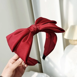Detailed close-up of a large red satin bow headband with elegant silky fabric texture