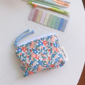 Detail of floral cotton coin pouch with a blue rope zipper pull and textile label