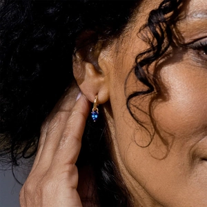 Close-up of model wearing gold C-shaped hoop earrings with blue heart crystal drops