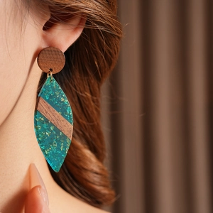 Macro d'une boucle d'oreille en bois et résine verte en forme de feuille sur mannequin