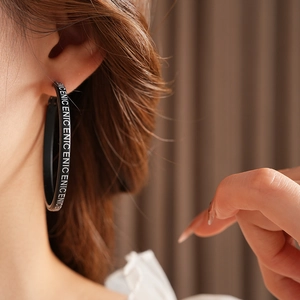 Gros plan de boucles d'oreilles rondes en cuir noir avec lettrage ENIC sur modèle