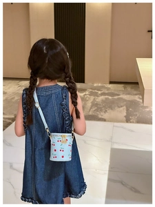 Detail of blue cherry print bucket bag with gold chain on a young girl in denim dress