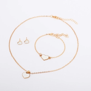 Detail shot of golden jewelry set featuring white heart pendants and lobster clasps