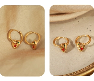 Detail of gold heart earrings with red and green enamel on premium satin background