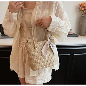 Close-up of beige woven texture handbag with decorative silk scarf on the handle