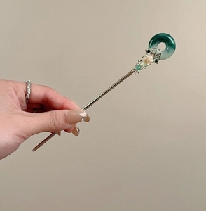 Détail d'épingle à cheveux argentée avec beignet de jade vert et fleur en métal