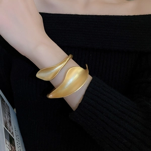 Detail of matte gold leaf cuff bracelet worn on wrist against black knit fabric