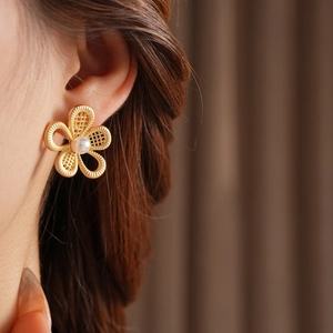 Gros plan détaillé de boucles d'oreilles fleur dorée avec perle blanche sur le modèle