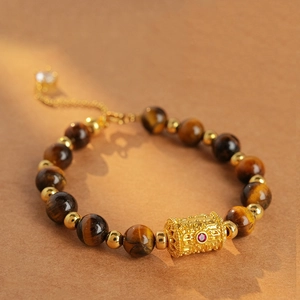 Detailed shot of tiger eye stone bracelet with golden hollow cylinder and red gemstone