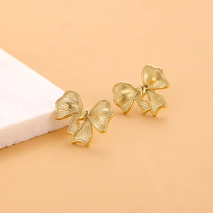 Détail de boucles d'oreilles nœud dorées sur fond de pierre blanche, plaqué or 18K