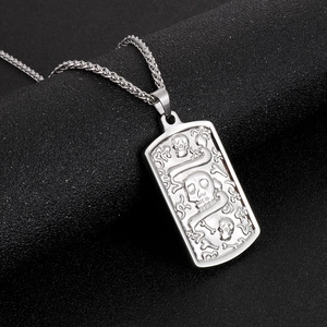 Macro detail of silver rectangular pendant with embossed skull, snake, and bone motifs