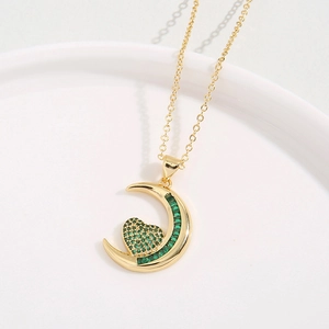 Golden crescent moon necklace with heart emerald zircon pendant on white plate