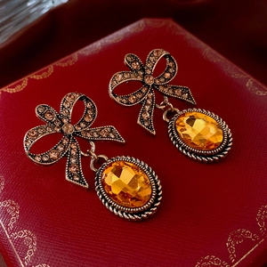 Macro shot of bow earrings with champagne rhinestones and amber stone on red leather box