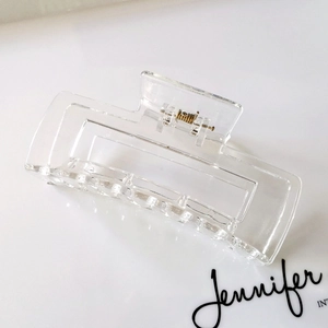 Detail view of transparent rectangular hair claw clip with golden metal spring mechanism