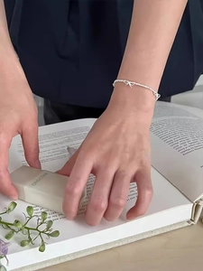 Bracciale in argento S925 con ciondoli a fiocco indossato tenendo un profumo
