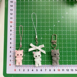 Close-up of pink, white, and grey flocked cat charms with bows on a measurement mat