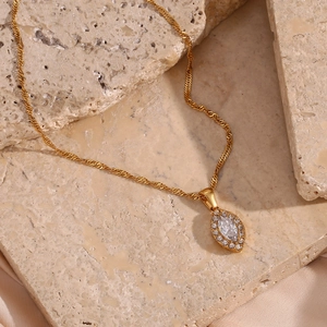 Detailed view of a gold leaf necklace with marquise zircon on beige marble and silk