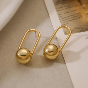 Detail view of U-shaped gold earrings with polished sphere pendant on textured surface
