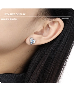 Detailed close-up of a silver heart-shaped earring with a blue crystal on model's ear