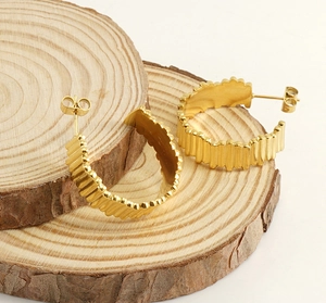 Detail of 18K gold-plated C-shaped earrings with wave texture on wood surface