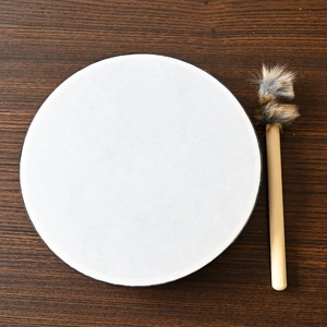 Top-down view of a Tree of Life shaman drum with a wooden mallet on a dark wood background