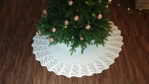 Close-up of white knitted Christmas tree skirt with hollow lace edge on wood floor