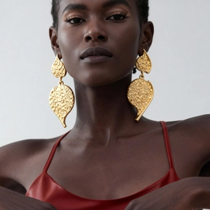 Golden large heart-shaped stud earrings with metallic wrinkled texture worn by a model