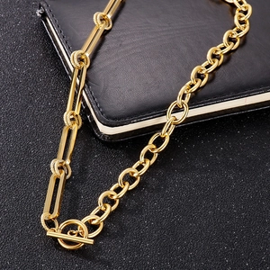 Detailed shot of golden OT buckle and chunky spliced link chain on black leather background