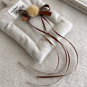 Detail of brown faux fur pom pom hair clip with elegant ribbons and quilted fabric base
