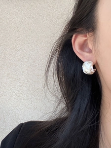 Macro view of silver C-shaped earrings with cross texture worn on a model's ear