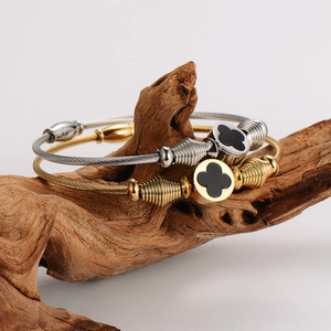 Two-tone wire cable bracelets with black clover charm displayed on a natural branch