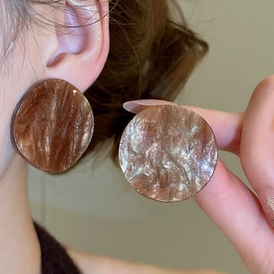 Macro detail of large acrylic resin hoop earrings with amber marble texture design