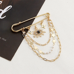 Detail of gold safety pin brooch with dangling chains, star charms, pearls and evil eye charm