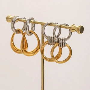 Two-tone stainless steel hoop earrings with gold geometric pendants on a metal stand