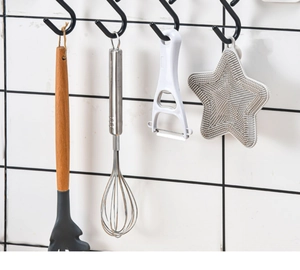 Detail of black S-shaped hooks holding various kitchen tools against a tiled wall