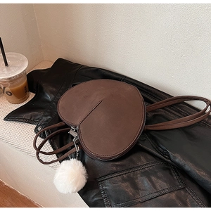 Detailansicht der herzförmigen Umhängetasche aus mattem Leder mit weißem Plüsch-Pompon-Anhänger