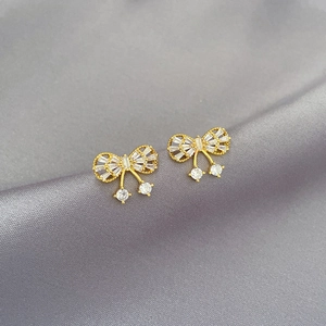 Detailed macro view of gold butterfly earrings with micro-pave crystals on grey silk