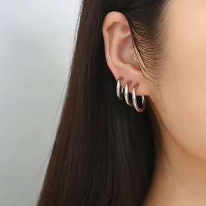 Gros plan de trois boucles d'oreilles clips en acier inoxydable sur l'oreille d'un modèle