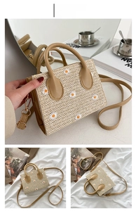 Detail view of khaki straw bag featuring white daisy embroidery and zipper closure