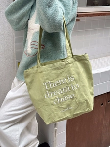 Close-up of light green canvas tote bag with dream to chase embroidered text