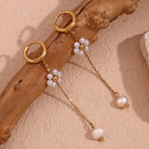 Detail of 18K gold-plated mini hoops with handmade pearl flowers on a wooden branch