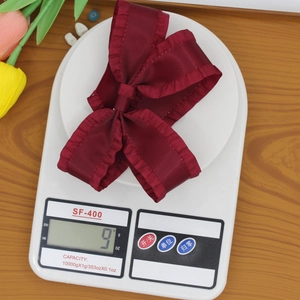 Elegant wine red satin bow hair clip with ruffle edges weighing 9g on a scale