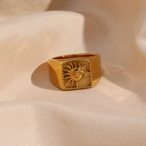 Detailed view of gold square signet ring with embossed sun face on soft beige silk