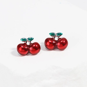 Gros plan de boucles d'oreilles cerises rouges émaillées sur une surface blanche