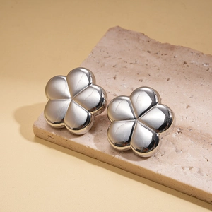 Close-up of silver metal flower earrings with a high-polish finish on a stone pedestal